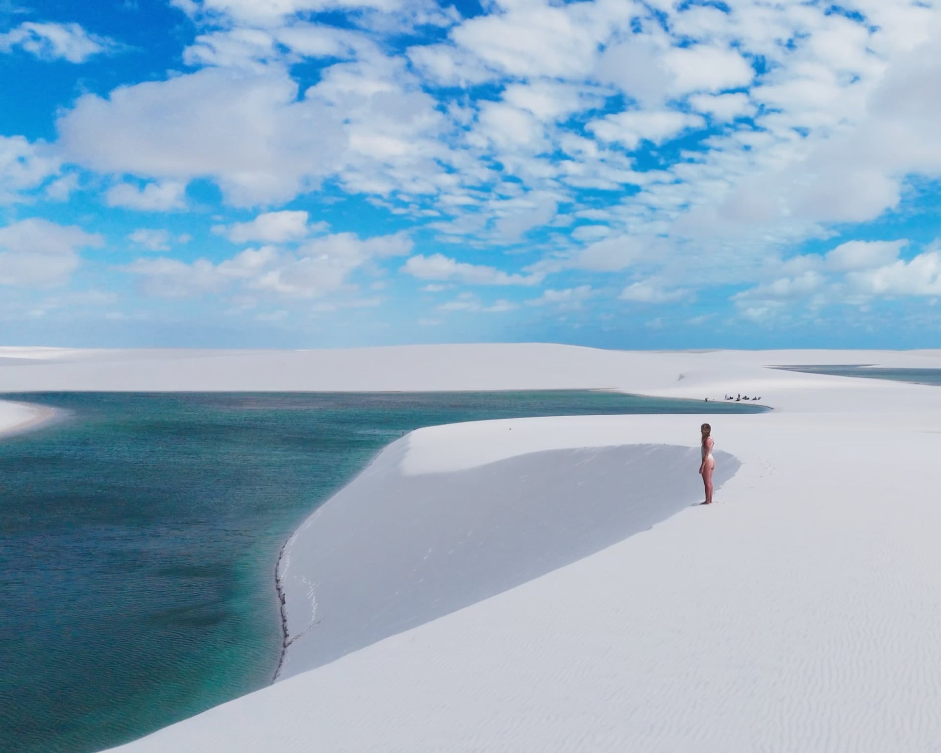 Woman standing on a white dune above a turquoise lagoon in Lençóis Maranhenses under a blue sky Woman standing on a white dune above a turquoise lagoon in Lençóis Maranhenses under a blue sky