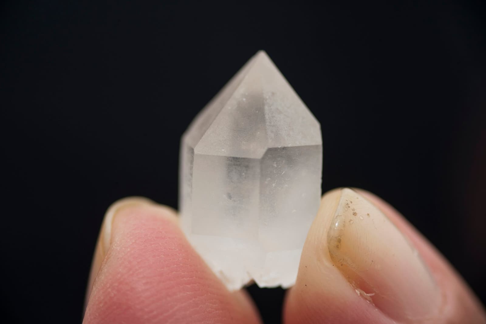 Picked up, turned over, put back down. The plateau grows these. Photo: Marcelo Andre A small clear quartz crystal point held between two fingers against a black background, found during a mount roraima expedition on the plateau