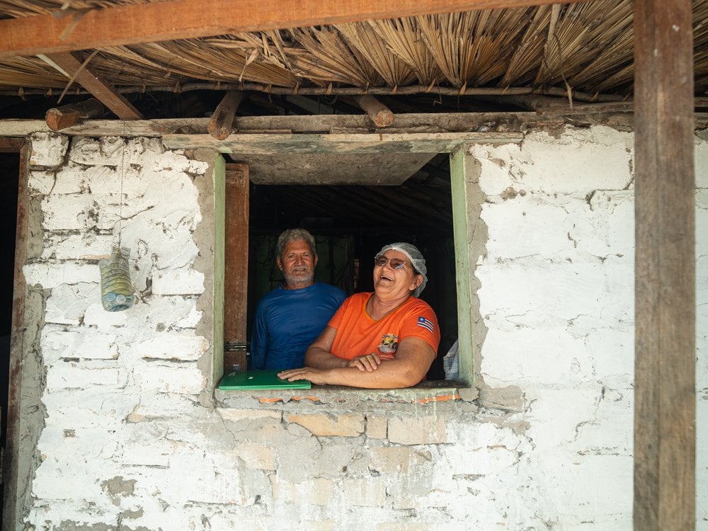 From fishermen to hosts: Dona Dete and Seu Moacir have seen their lives transform thanks to income from tourism in the Baixa Grande oasis. (Credit: Marcelo Bonifácio) Dona Dete and Seu Moacir smiling at the window of their home in the Baixa Grande oasis