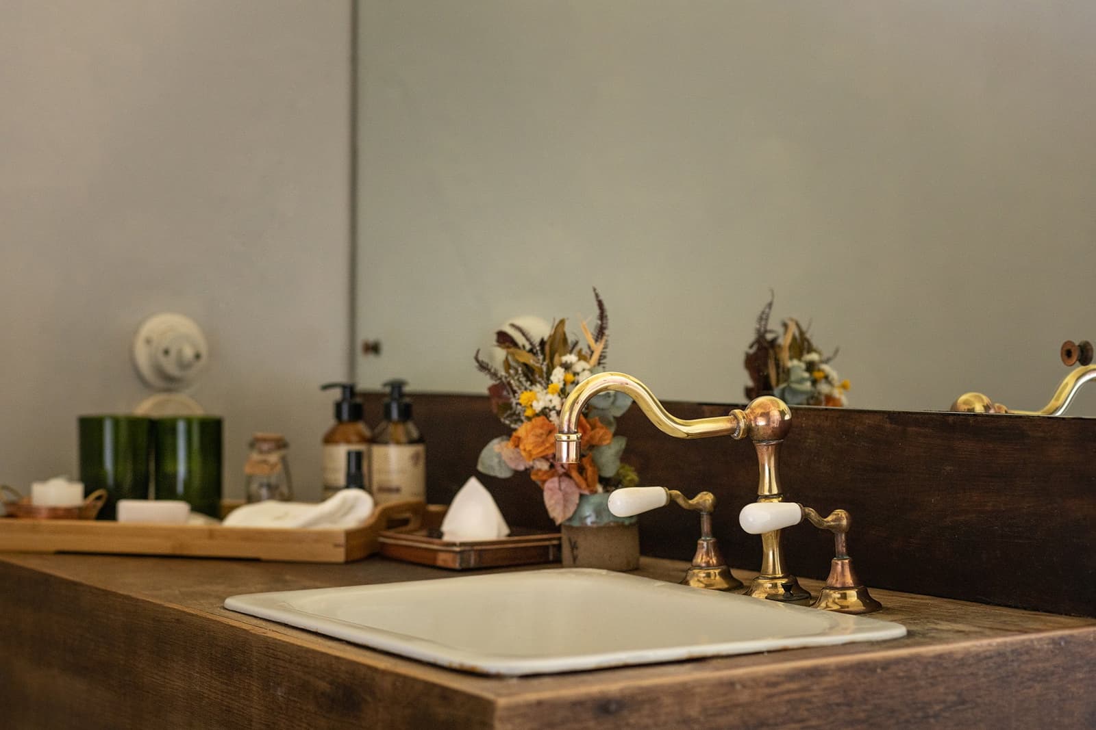Comfort that earns its place, one thoughtful detail at a time. Photo: Henrique Mangeon Close-up of a white ceramic sink set into a dark wood countertop with brass vintage-style faucet handles and a small dried-flower arrangement at the Ibiti Project's Engenho Lodge bathroom