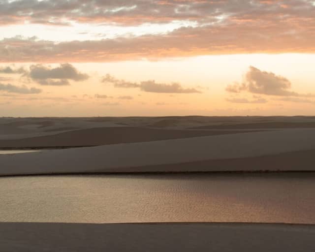 Pink sunset sky over the white sand dunes and a rainwater lagoon in Lençóis Maranhenses