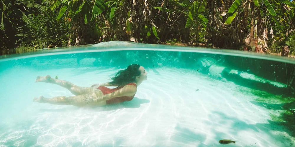 A woman swims underwater in a vibrant turquoise fervedouro natural pool during a Jalapão adventure.