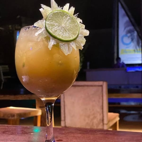 A chilled, yellow cocktail garnished with a lime wheel sits on a wooden bar table at night, offering a relaxing evening drink during a Jalapão adventure