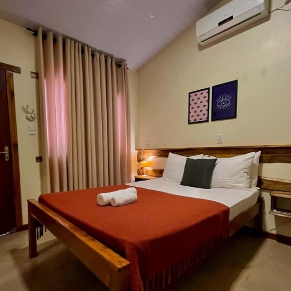 Cozy guesthouse bedroom featuring a double bed with a red blanket, rustic wooden headboard, and air conditioning for a comfortable stay in Jalapão.