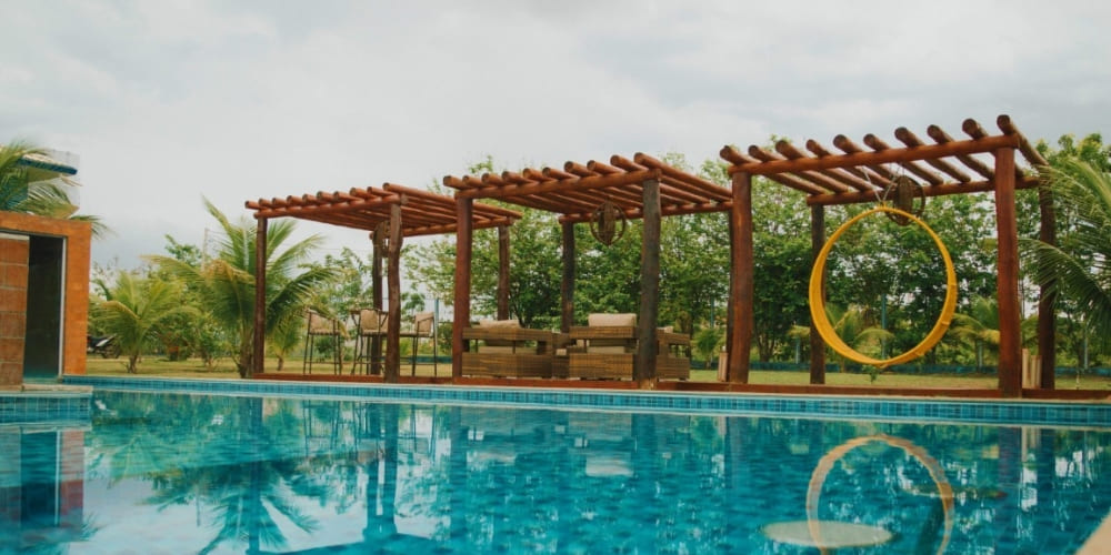 A large swimming pool lined with wooden pergolas and a yellow swing chair at a Jalapão guesthouse