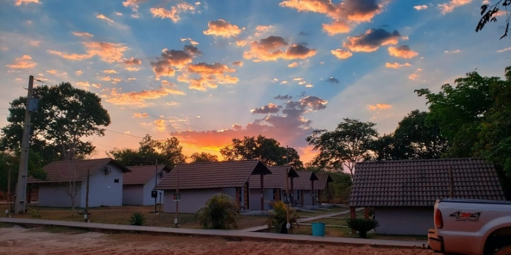 Small guesthouse cabins lined up under a vibrant pink and orange sunset sky in São Félix do Tocantins.