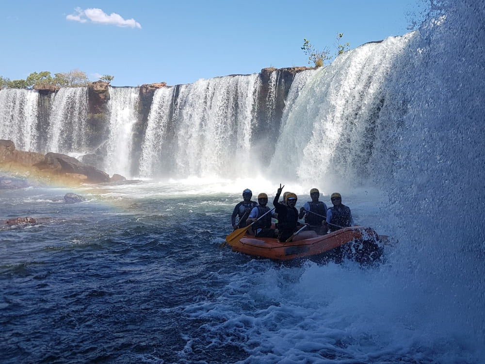 A group of tourists in an orange raft experiences the powerful Cachoeira da Velha waterfall in Jalapão.
