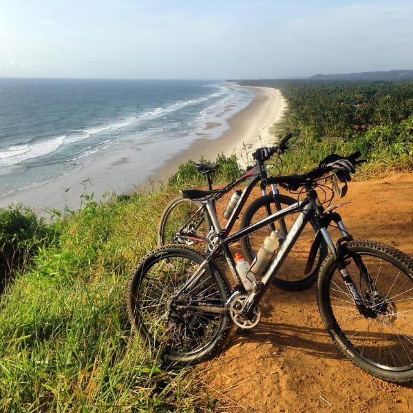 Two mountain bikes are parked on a dirt trail on a cliffside, offering a scenic view of the coastline.