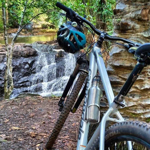 A mountain bike rests near a small waterfall surrounded by the lush Atlantic Forest.