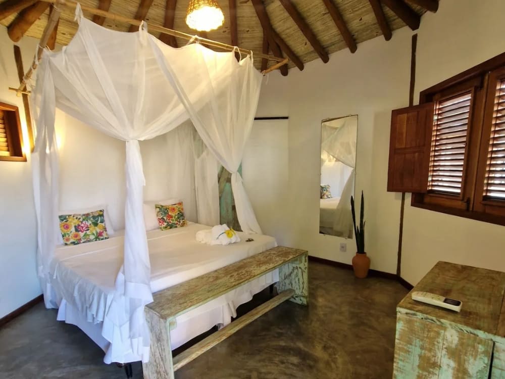A rustic, charming bedroom features a canopy bed draped with white mosquito netting and distressed wooden furniture.