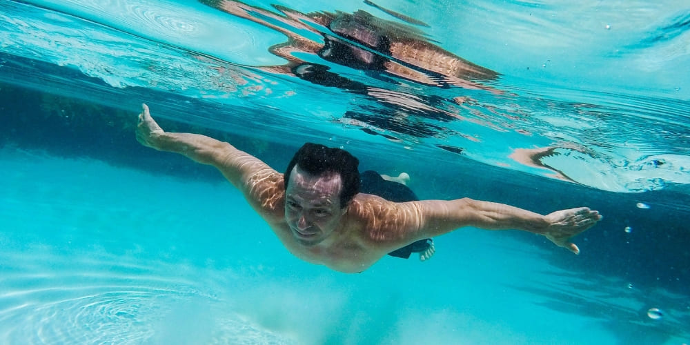Man swimming underwater in bright blue, clear waters of a fervedouro during a Jalapão trek.
