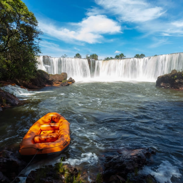 Orange raft floating on a river with a wide waterfall in the background in Jalapão Brazil.