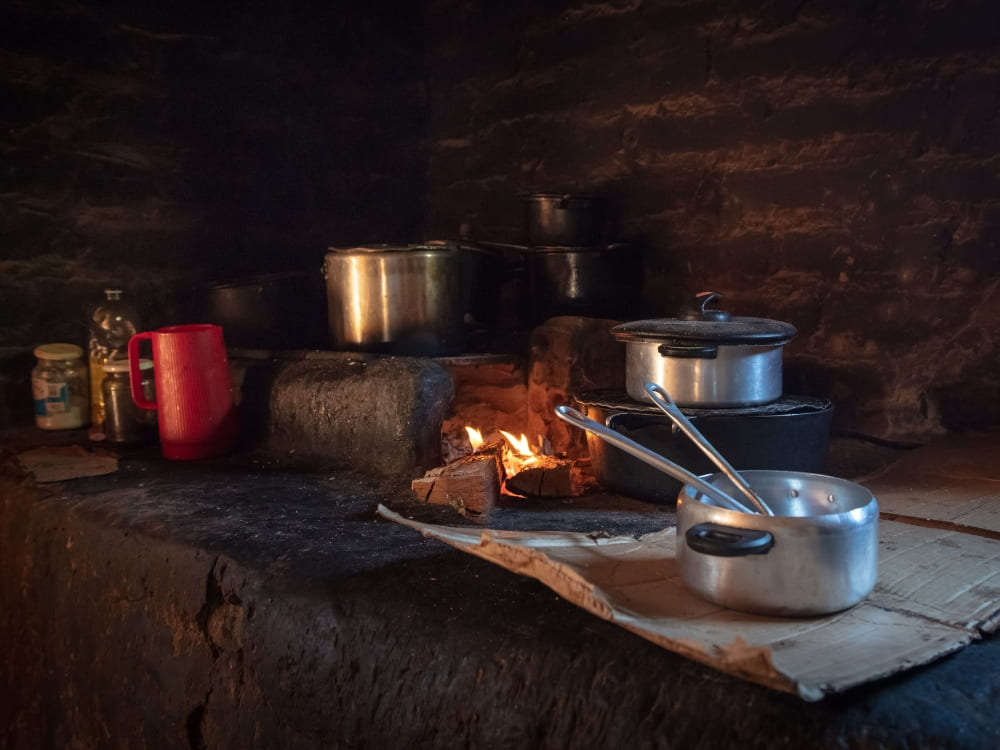 Traditional aluminum pots on a rustic wood-burning stove over an open fire preparing local cuisine.
