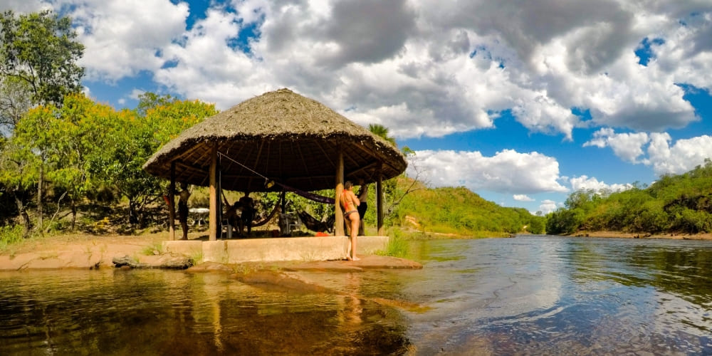 Rustic thatched-roof gazebo beside a calm river where trekkers relax during a Jalapão trek.