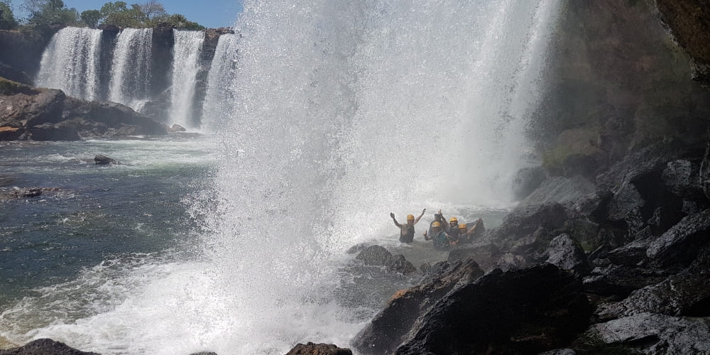 Group of adventurers in a raft navigating thrilling river rapids beneath a massive waterfall.