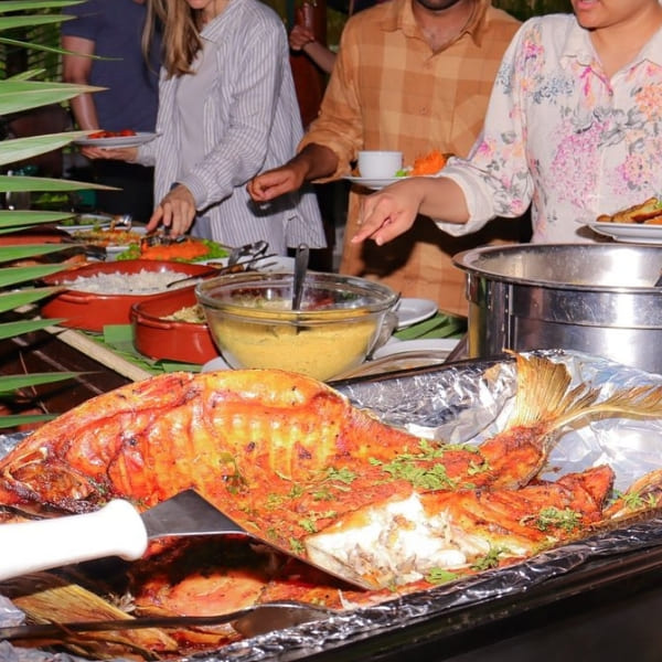 Tourists serving themselves at the lodge buffet featuring a large roasted regional fish on a tray.