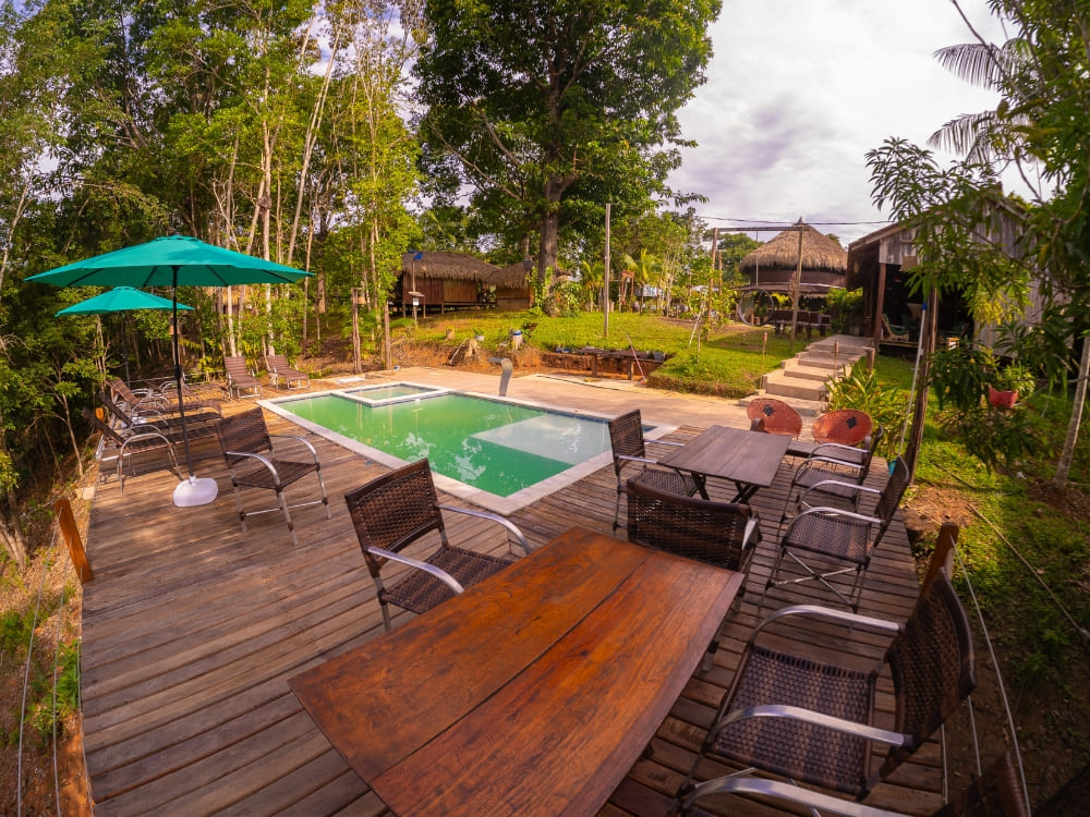 Spacious wooden deck with tables, chairs, and a rectangular swimming pool surrounded by nature at the Amazon Turtle Lodge.