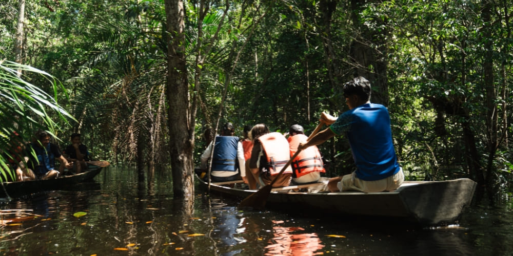 Group of tourists wearing life jackets navigating a canoe through a flooded Amazon forest.