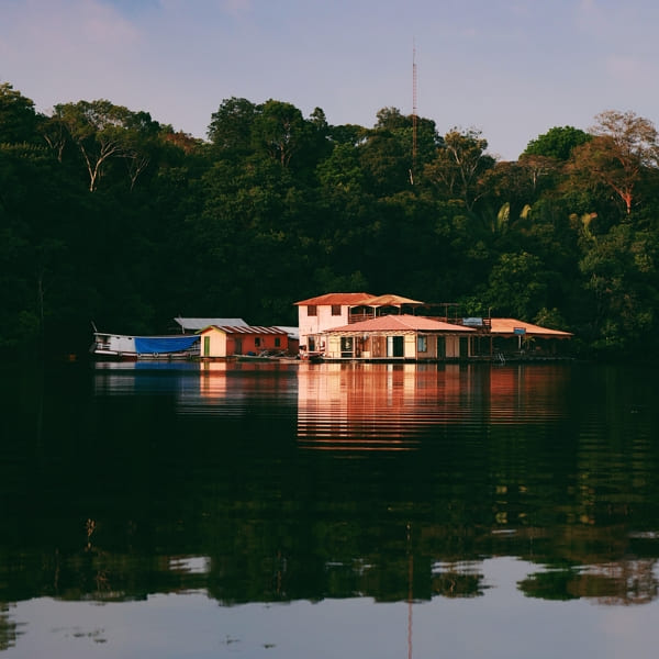 Typical floating house anchored in calm river waters surrounded by Amazonian vegetation.