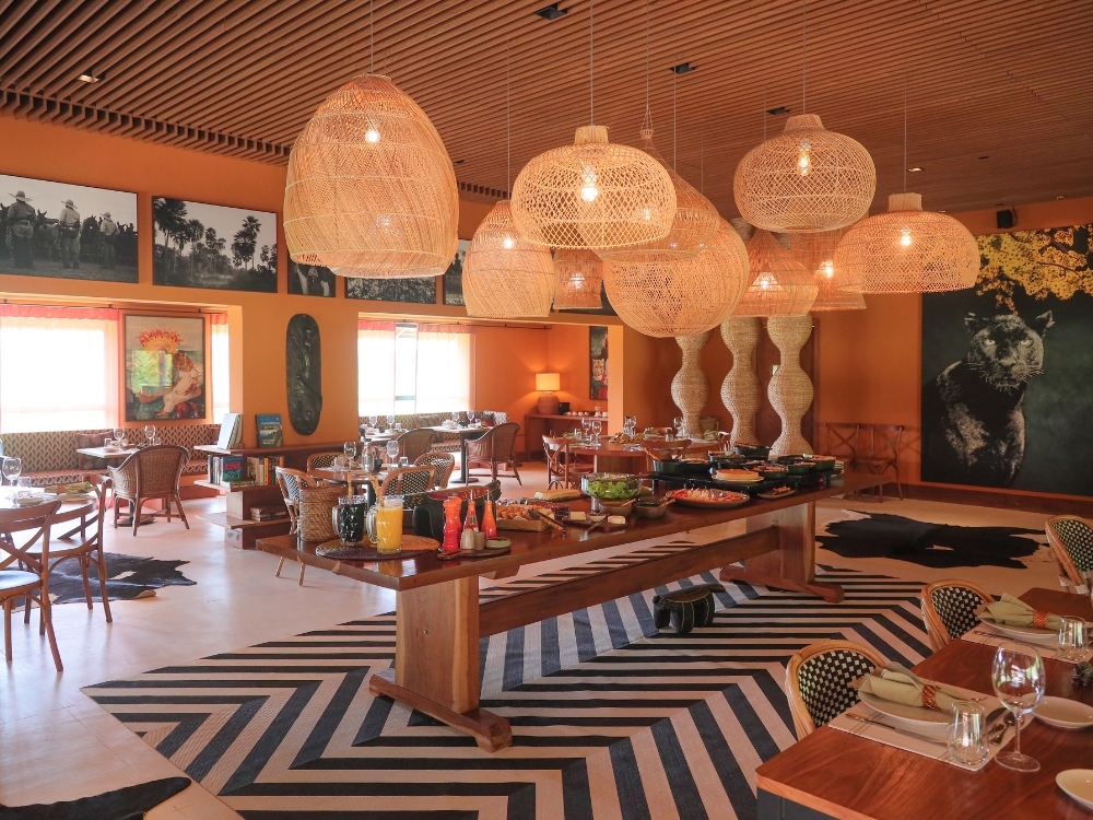 The dining room at Caiman Ecolodge showing a long buffet table, a zebra print rug, and wicker chandeliers.