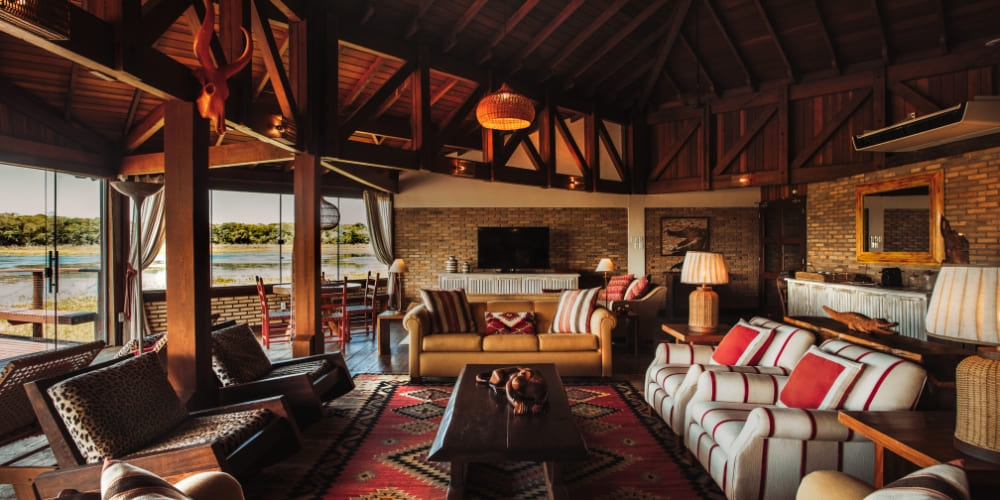 A spacious rustic living room at Caiman Ecolodge with sofas, a large wooden table, and scenic views.