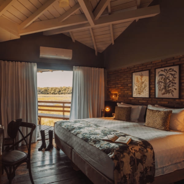 A luxury suite bedroom with a large bed, exposed brick walls, and an outdoor terrace overlooking the wetlands.