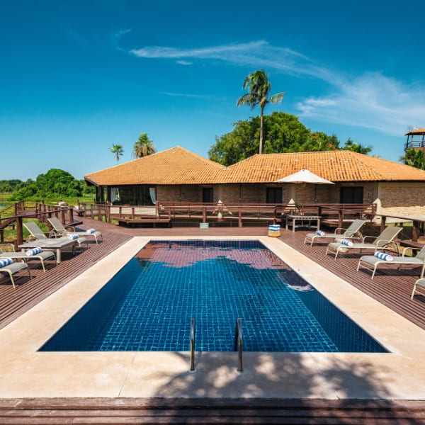 The Private Villa at Caiman featuring a wooden deck, lounge chairs, and a swimming pool overlooking nature.
