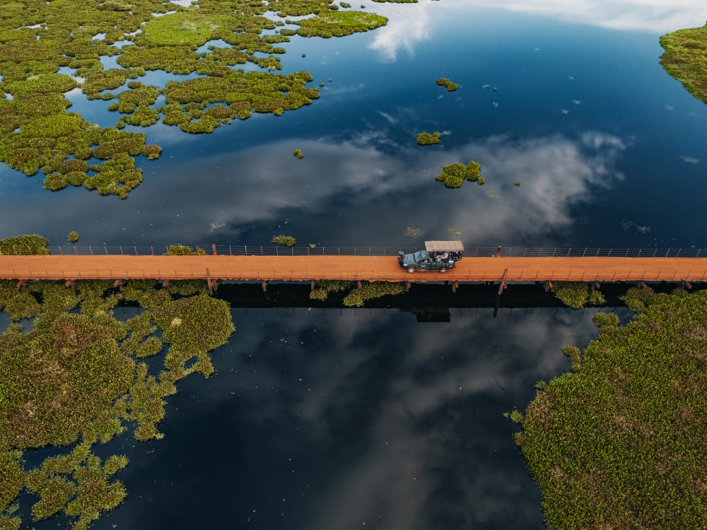 Aerial view of a safari jeep crossing a long wooden bridge over the flooded plains of the Pantanal.