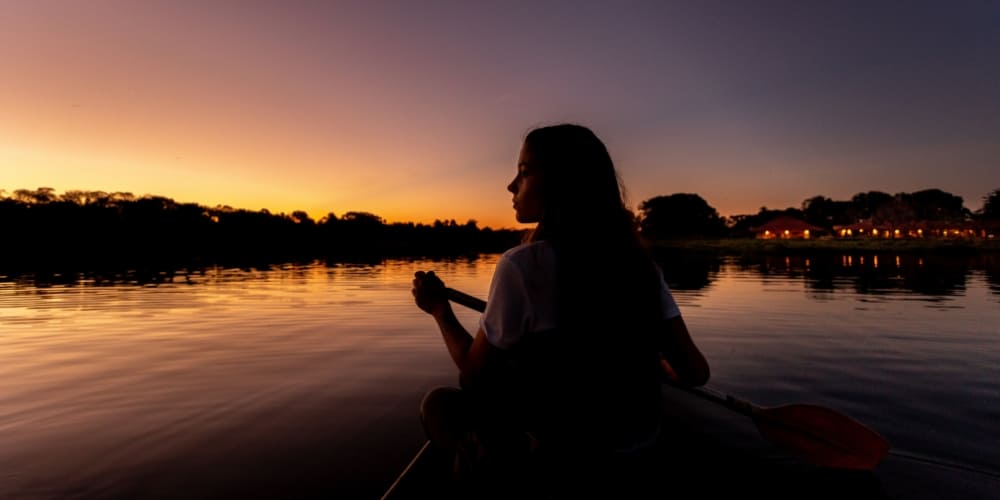 Silhouette d'une femme faisant du canoë sur une rivière calme contre un coucher de soleil orange vibrant au Pantanal.