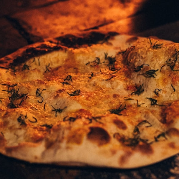 A freshly baked artisanal pizza with melted cheese and herbs, prepared in a wood-fired oven at Caiman.