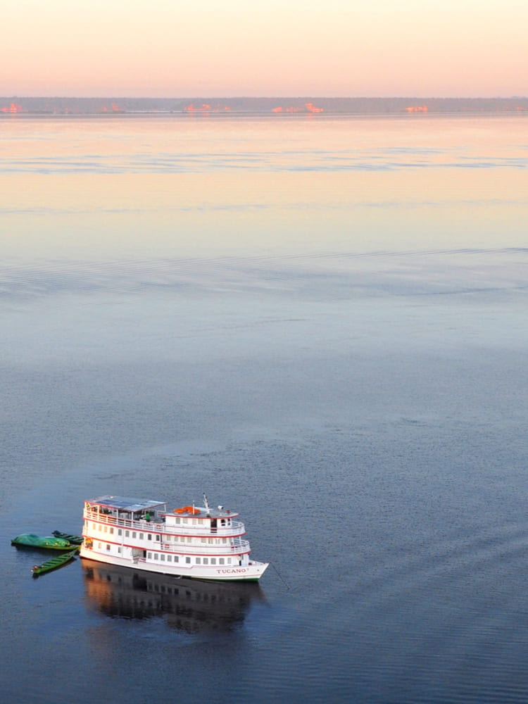 The white expedition vessel anchored on a wide river at dawn during an Amazon cruise from Manaus.