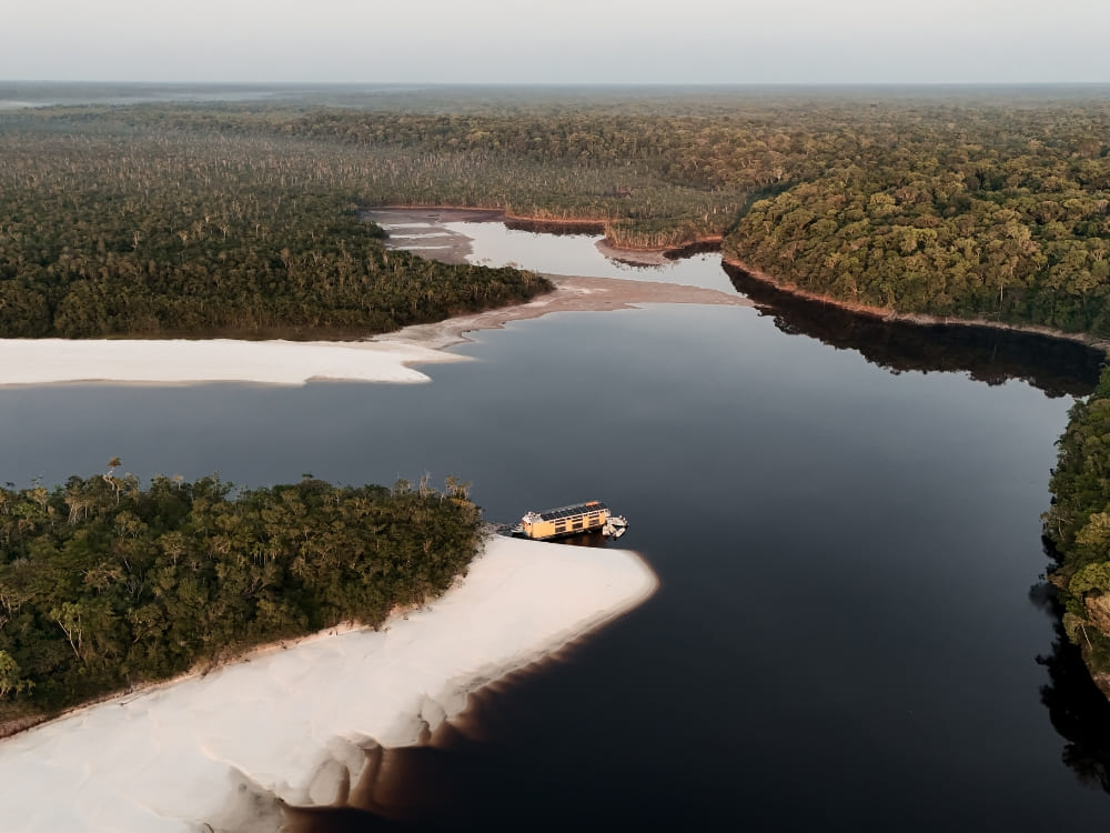 Aerial view of a river cruise in the Amazon Rainforest navigating between dense green forests and white-sand beaches.