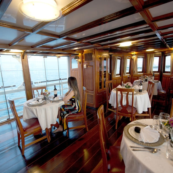 A woman sitting at a set table in the elegant wood-paneled dining room of the Tucano Amazon river cruise.
