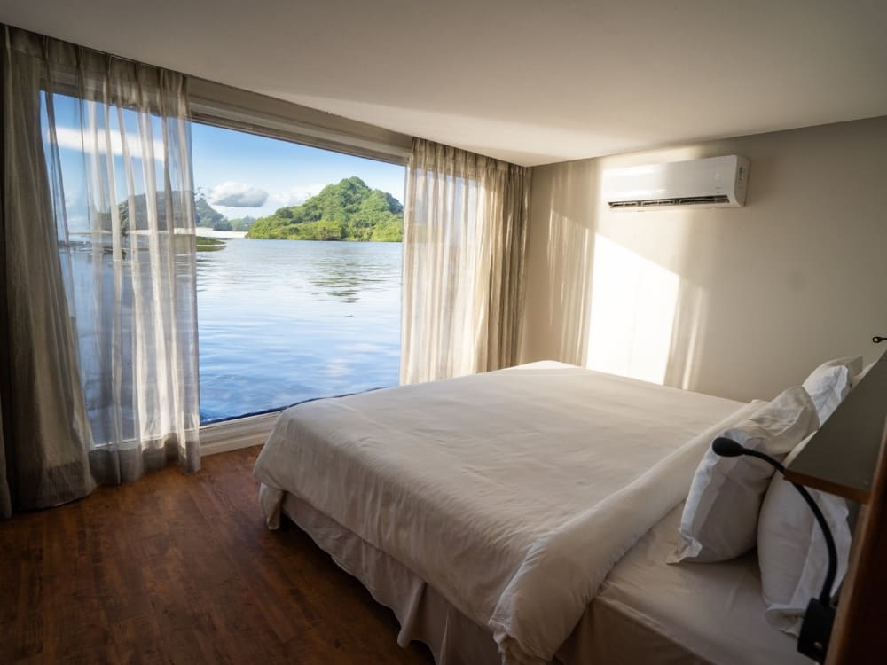 High-end accommodation on a luxury Amazon river cruise from Manaus, Brazil featuring a comfortable bed and floor-to-ceiling windows.