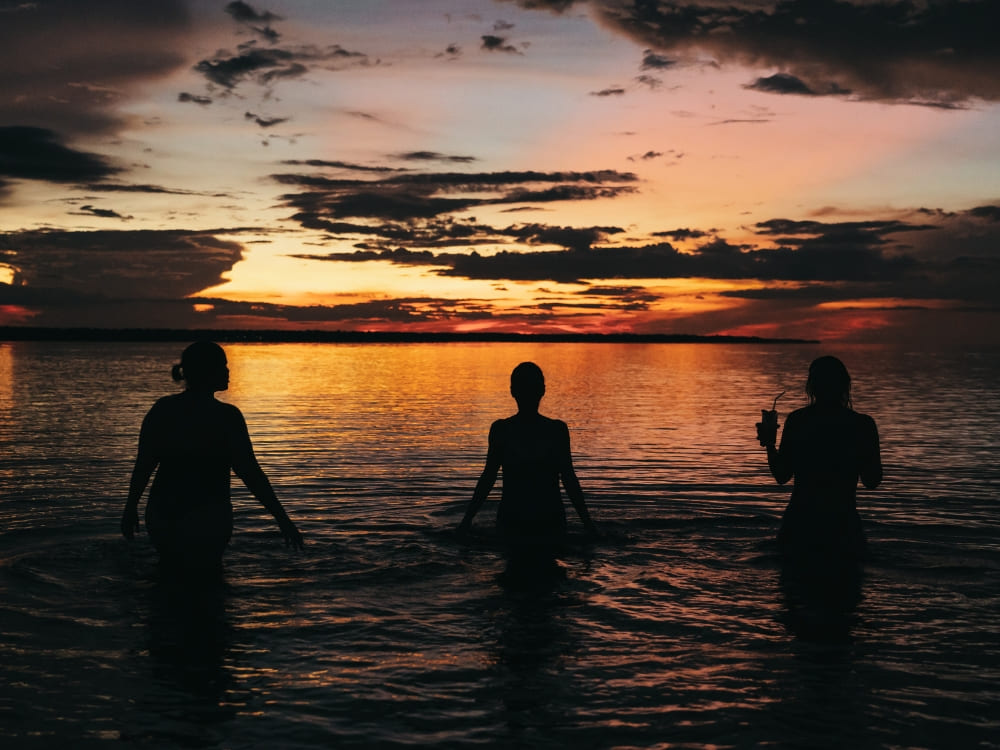 Silhouettes of three people enjoying a relaxing swim in the Negro River and sunset contemplation.