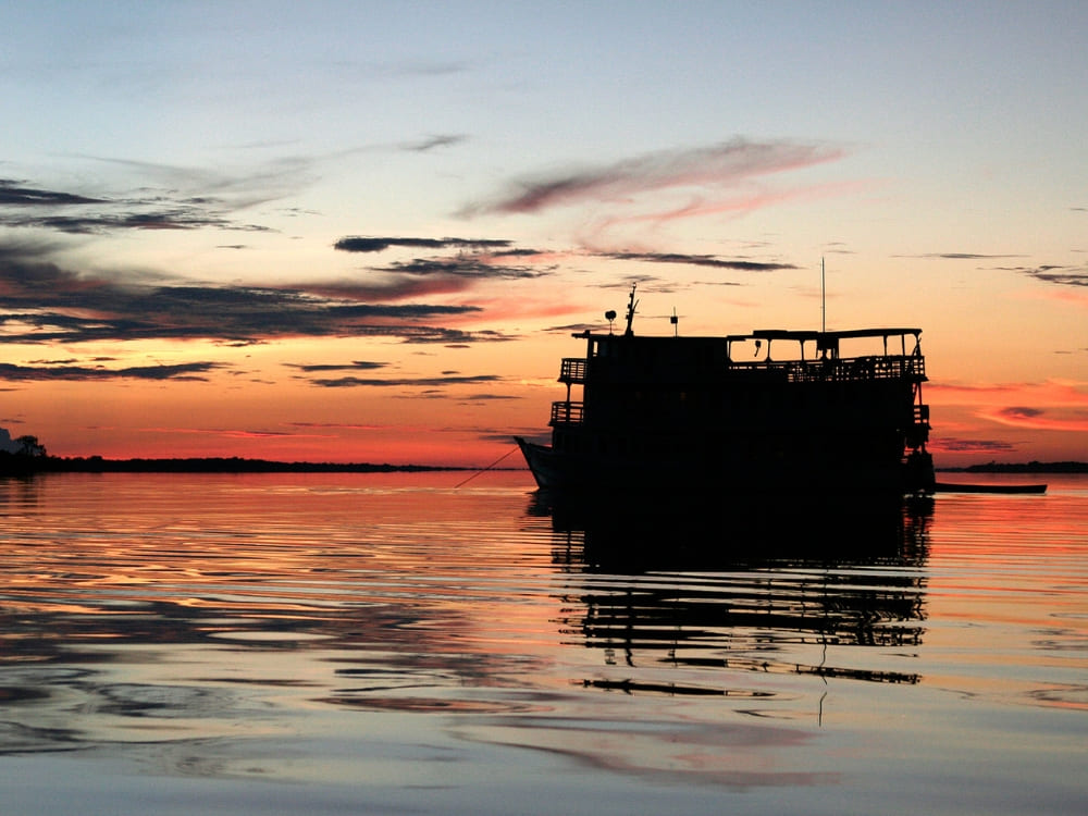  Silhouette of the three-floor riverboat reflecting on the water during a bright orange Amazonian sunset.