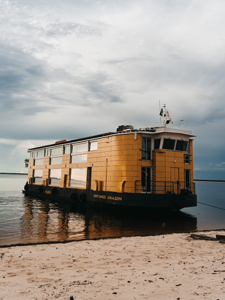 The Untamed Amazon Cruise docked at one of the nearby river beaches under a cloudy sky.