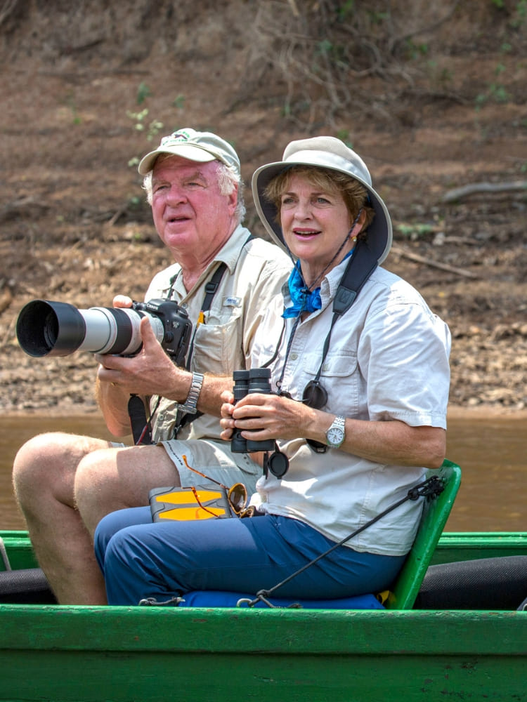 A smiling couple holding professional cameras and binoculars while riding a small expedition boat.