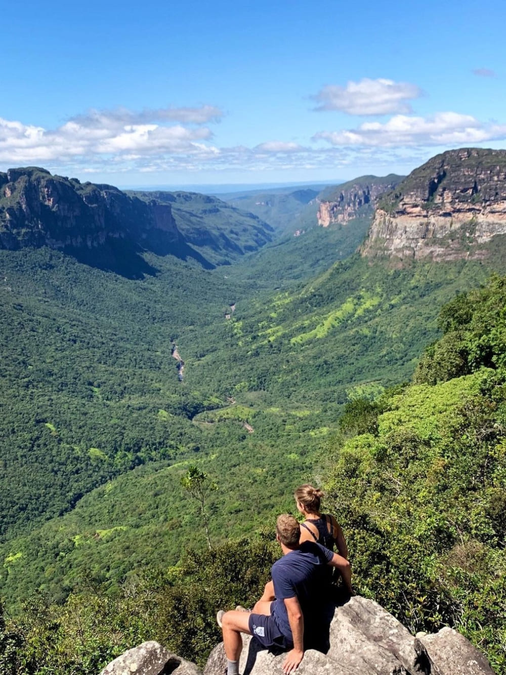 Two hikers sit on a rocky cliff admiring the vast, green expanse of Vale do Pati in Chapada Diamantina National Park. Two hikers sit on a rocky cliff admiring the vast, green expanse of Vale do Pati in Chapada Diamantina National Park.