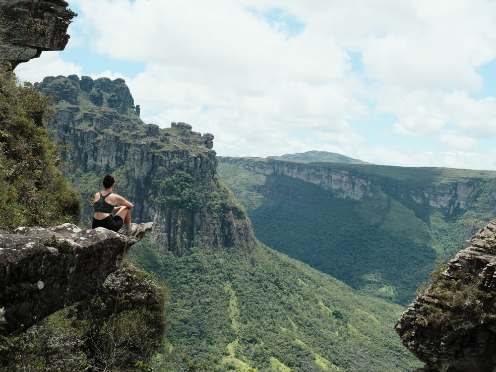 A backpacker sits on a jagged rock ledge enjoying a panoramic view of the steep cliffs and pristine green valleys of Vale do Pati. A backpacker sits on a jagged rock ledge enjoying a panoramic view of the steep cliffs and pristine green valleys of Vale do Pati.