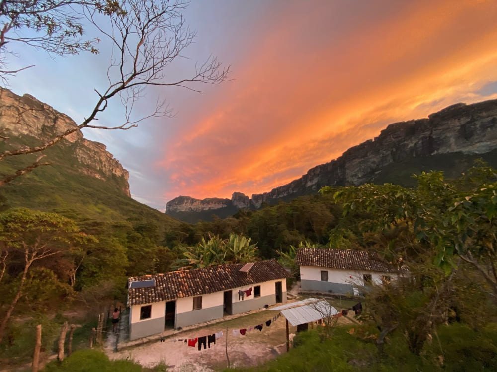 Modest local houses equipped with solar panels sit in a lush green valley beneath a colorful sunset sky in Vale do Pati. Modest local houses equipped with solar panels sit in a lush green valley beneath a colorful sunset sky in Vale do Pati.