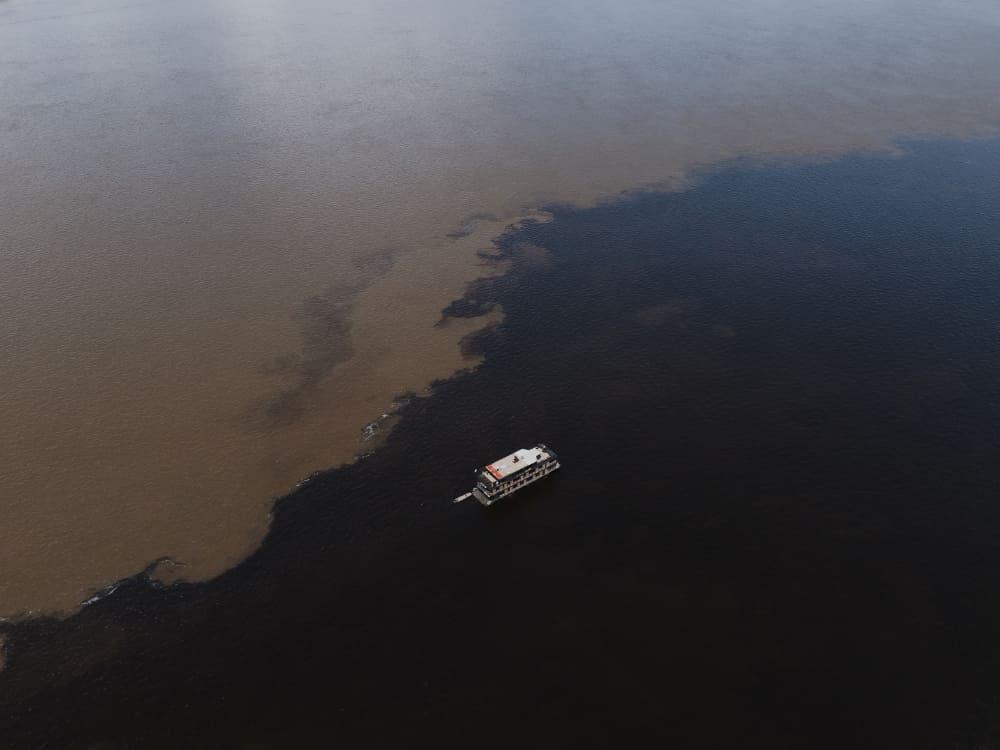 Um barco navegando no Encontro das Águas, onde o Rio Negro preto e o Rio Solimões marrom fluem lado a lado sem se misturar.