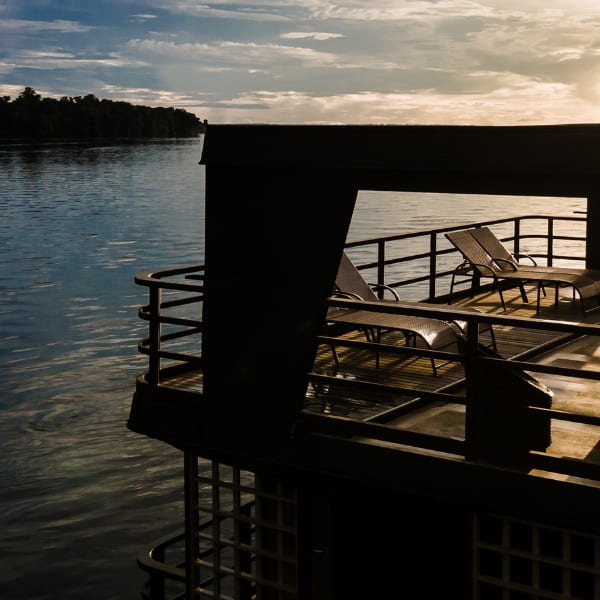 Viewing deck of an Amazon river cruise boat with lounge chairs facing the water at sunset.
