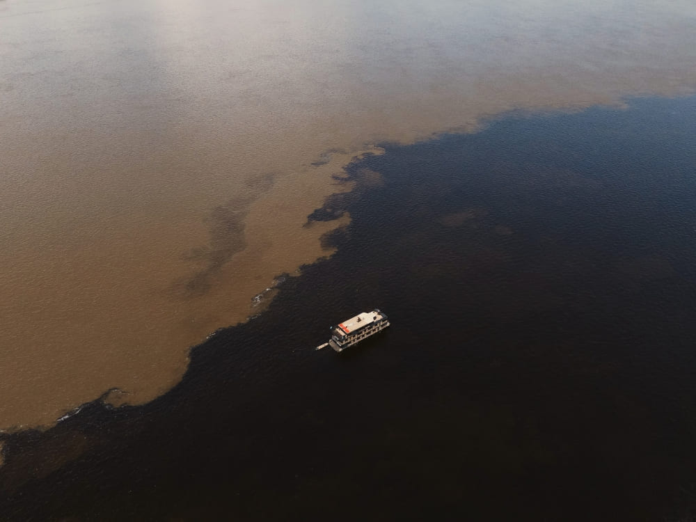 Aerial view of a riverboat navigating the Meeting of the Waters in the Amazon, showing the distinct dark and sandy rivers flowing side-by-side.