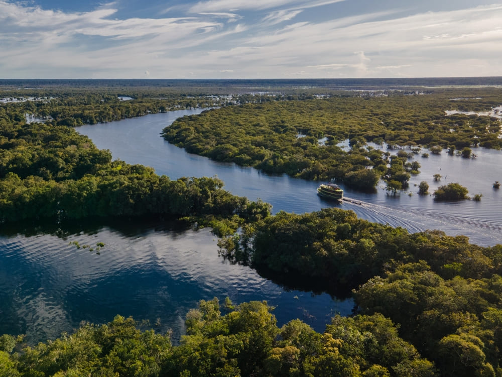 Aerial view of a Katerre riverboat navigating the winding channels of the Negro River in the Amazon Rainforest, surrounded by lush green vegetation.