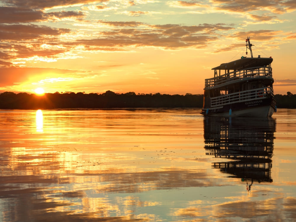 Traditional wooden riverboat navigating the calm Amazon waters during a golden sunset reflecting on the river. Traditional wooden riverboat navigating the calm Amazon waters during a golden sunset reflecting on the river.