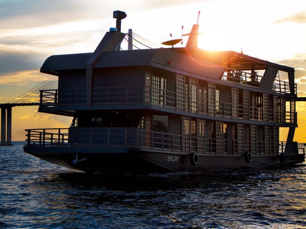 The Zaltana luxury riverboat anchored in the Amazon river at sunset, showing its modern design and spacious structure for a premium cruise.
