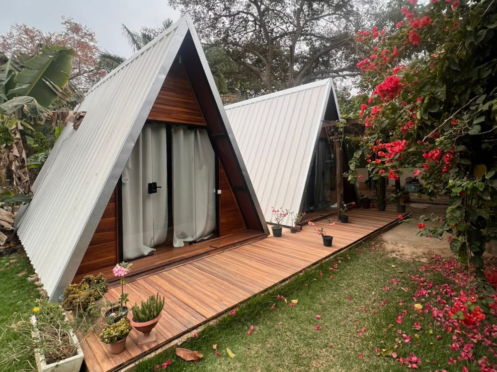 Two rustic A-frame wooden chalets sit at Berço Pantaneiro in Porto Jofre, surrounded by bright pink flowers.