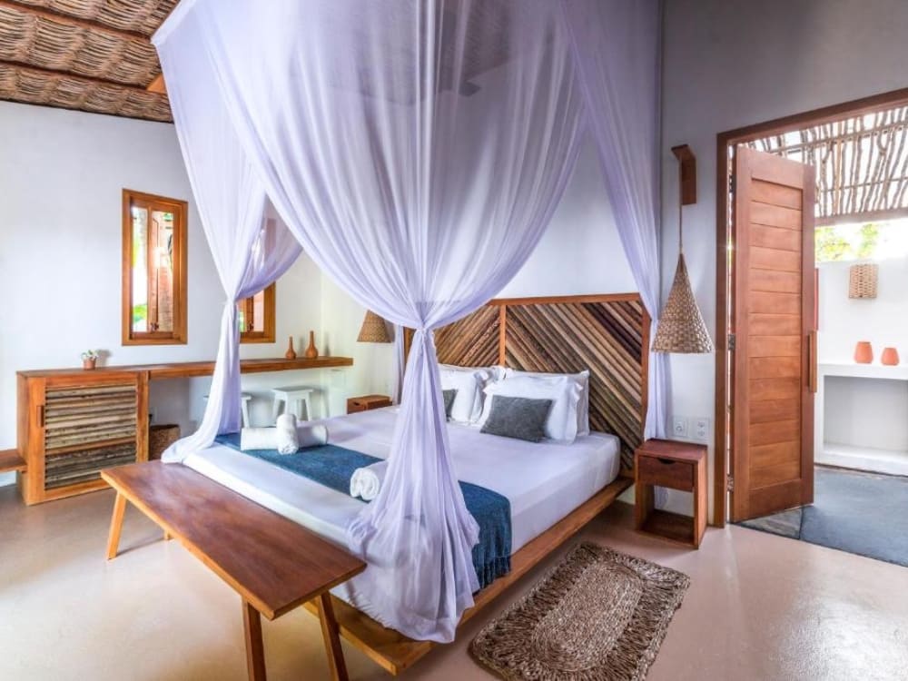 Elegant and bright interior of a chalet at Muita Paz inn, focused on a double bed covered by a large translucent mosquito net.