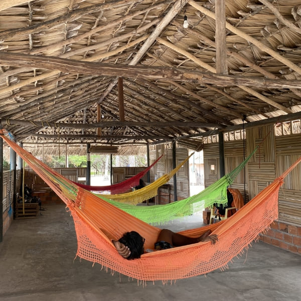 Eine traditionelle Strohhütte steht auf weißem Sand, umgeben von üppigem grünen Laub und hohen Palmen unter einem strahlend blauen Himmel.